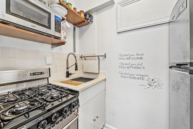 kitchen with open shelves, a sink, decorative backsplash, light countertops, and stainless steel appliances