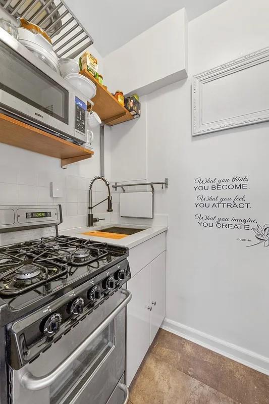 kitchen featuring baseboards, open shelves, a sink, stainless steel appliances, and backsplash