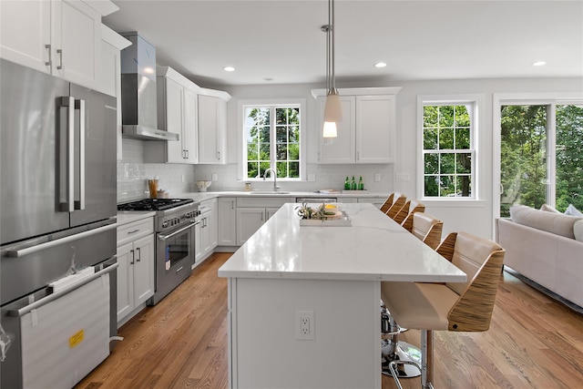 kitchen featuring light wood-style flooring, a sink, appliances with stainless steel finishes, a kitchen breakfast bar, and wall chimney exhaust hood