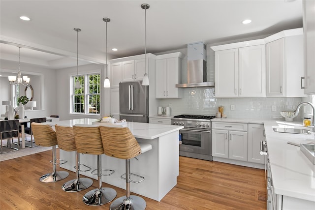 kitchen with premium appliances, light wood-style flooring, wall chimney range hood, and a sink