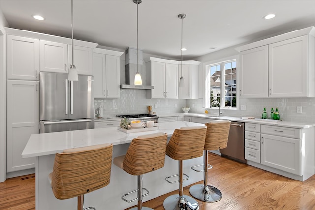 kitchen featuring wall chimney range hood, stainless steel appliances, light wood-style floors, white cabinetry, and a sink