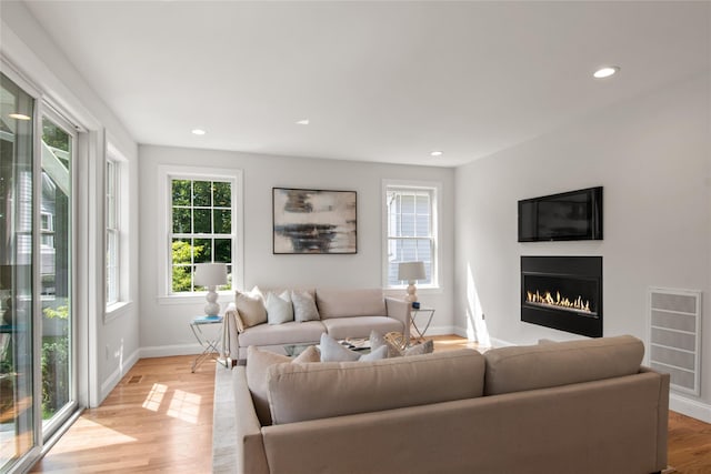 living room featuring light wood finished floors, recessed lighting, a lit fireplace, and baseboards