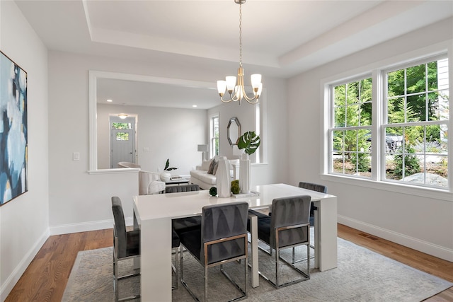 dining room featuring visible vents, a tray ceiling, wood finished floors, an inviting chandelier, and baseboards