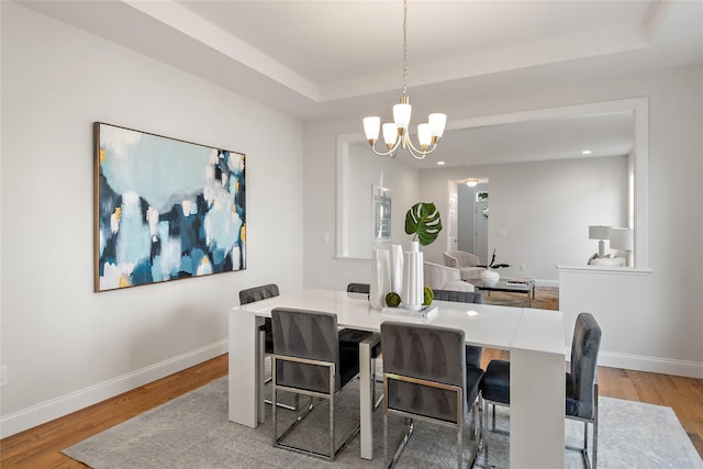 dining room featuring baseboards, a raised ceiling, a notable chandelier, and light wood-style flooring