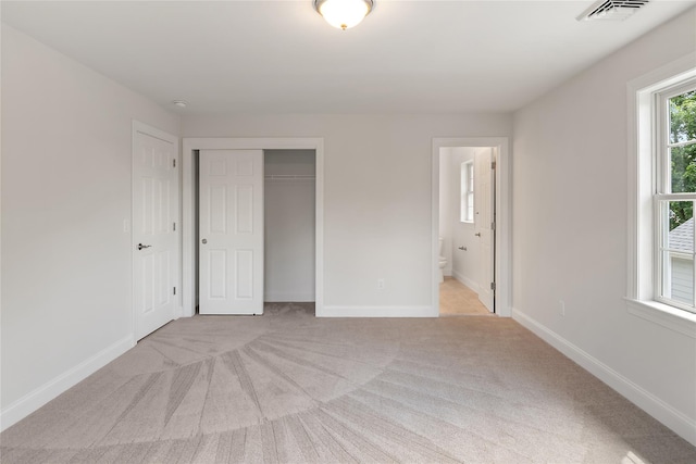 unfurnished bedroom with visible vents, light carpet, ensuite bathroom, a closet, and baseboards