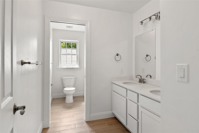 full bathroom with baseboards, toilet, double vanity, wood finished floors, and a sink