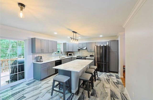 kitchen with gray cabinetry, under cabinet range hood, a kitchen breakfast bar, stainless steel appliances, and a sink