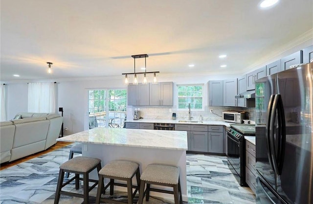 kitchen featuring a breakfast bar area, gray cabinets, a sink, black appliances, and open floor plan