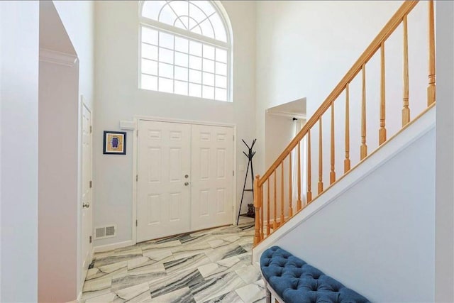 foyer featuring stairs, visible vents, marble finish floor, and a towering ceiling