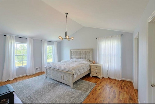 bedroom with visible vents, baseboards, a chandelier, vaulted ceiling, and wood finished floors