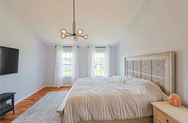 bedroom with vaulted ceiling, wood finished floors, baseboards, and a chandelier