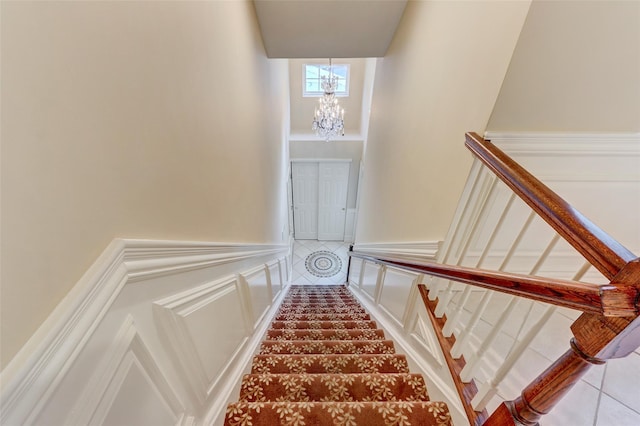 stairway featuring an inviting chandelier, a decorative wall, and a wainscoted wall