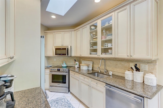 kitchen with a sink, tasteful backsplash, stainless steel appliances, a skylight, and light stone countertops