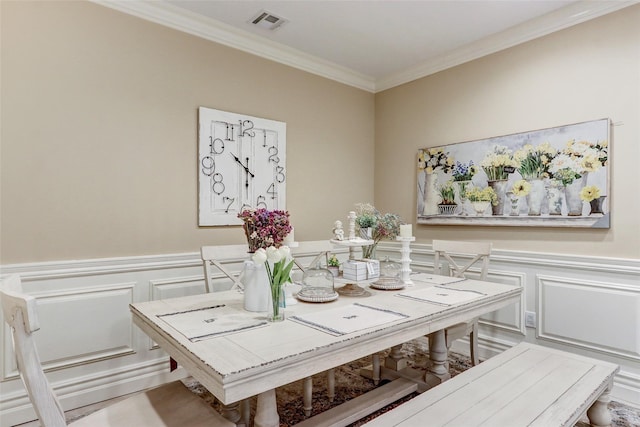 dining area with a wainscoted wall, visible vents, ornamental molding, and a decorative wall