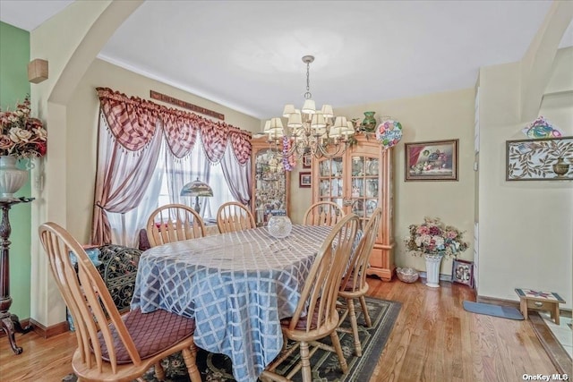 dining room featuring light wood-style flooring, baseboards, arched walkways, and a chandelier