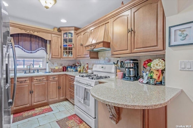 kitchen with custom range hood, white gas range oven, decorative backsplash, freestanding refrigerator, and a sink