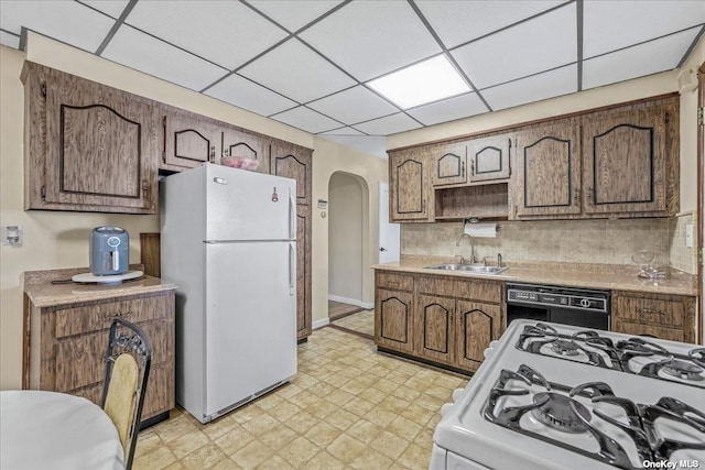 kitchen featuring light floors, light countertops, arched walkways, white appliances, and a sink