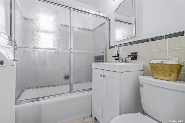 full bathroom with combined bath / shower with glass door, vanity, toilet, and tile walls