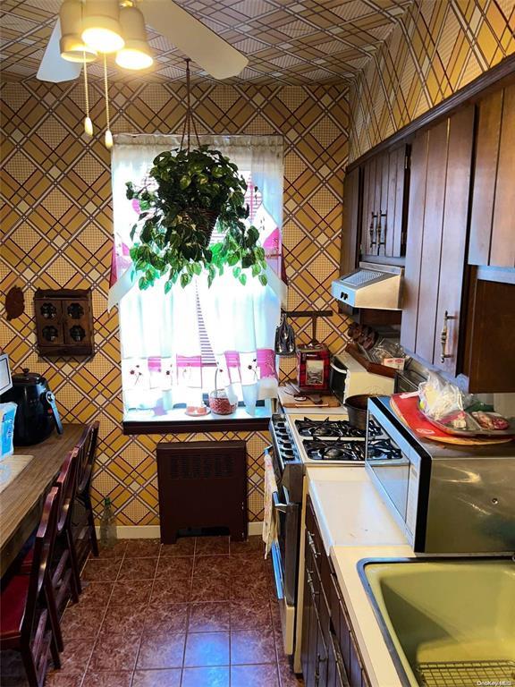 kitchen with a ceiling fan, a sink, exhaust hood, stainless steel gas range oven, and dark tile patterned floors