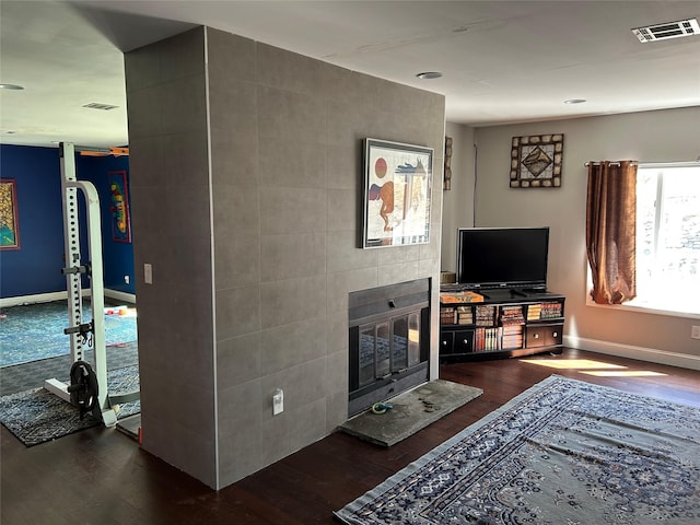 living area with a glass covered fireplace, visible vents, baseboards, and dark wood-style floors