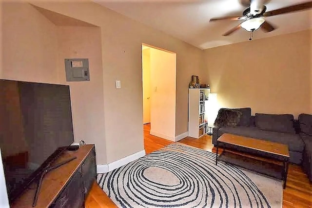 living area with electric panel, baseboards, light wood-type flooring, and a ceiling fan