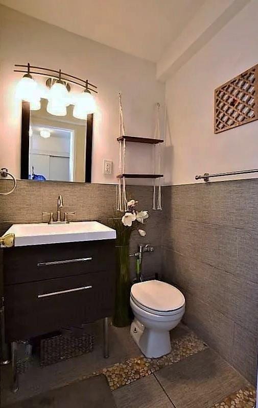 half bathroom featuring vanity, tile patterned flooring, wainscoting, tile walls, and toilet