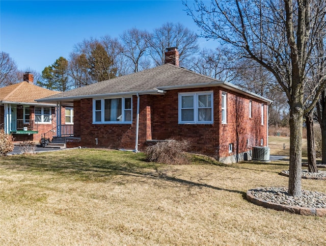 view of front facade with roof with shingles, a chimney, a front lawn, central air condition unit, and brick siding