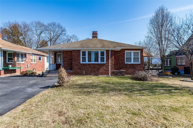 view of front of house featuring brick siding, a front lawn, roof with shingles, a chimney, and driveway