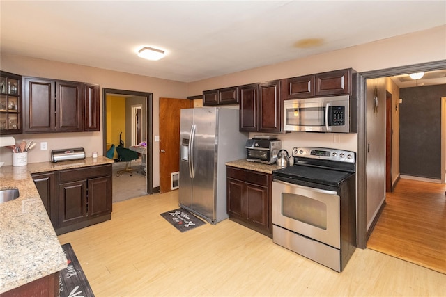 kitchen with dark brown cabinetry, glass insert cabinets, light wood-type flooring, and stainless steel appliances