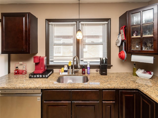 kitchen with glass insert cabinets, light stone countertops, dark brown cabinetry, dishwasher, and a sink