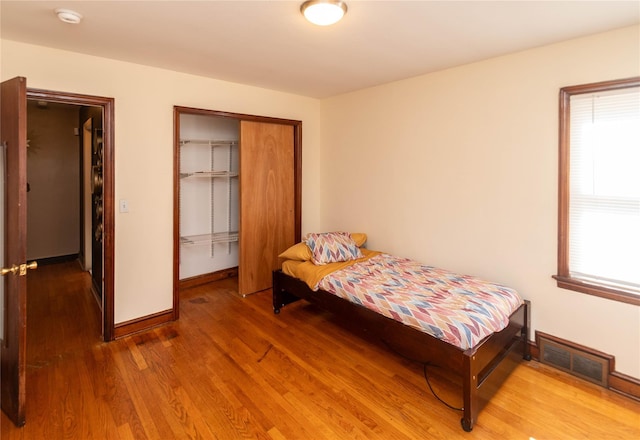 bedroom with wood finished floors, visible vents, a closet, and baseboards