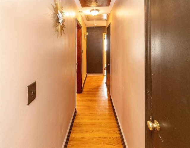 hallway featuring baseboards, visible vents, attic access, and light wood-style floors