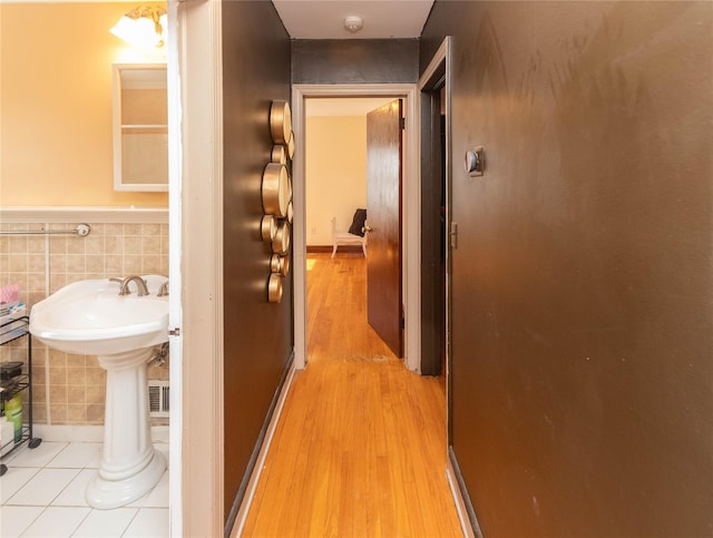 hall with a wainscoted wall, ornate columns, light wood finished floors, a sink, and tile walls