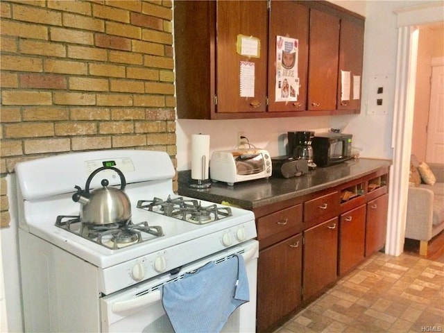 kitchen with dark countertops, brick wall, brown cabinetry, black microwave, and white gas range