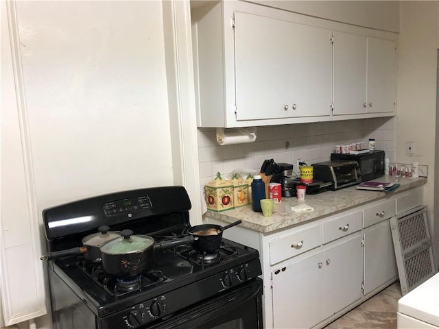 kitchen featuring decorative backsplash, white cabinets, gas stove, and light countertops