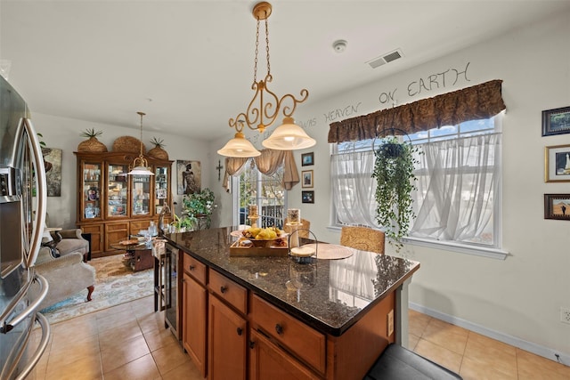 kitchen featuring dark stone countertops, light tile patterned floors, visible vents, a kitchen island, and stainless steel fridge