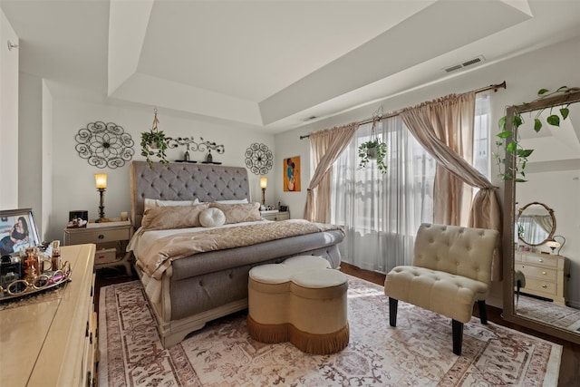 bedroom featuring a tray ceiling, visible vents, and wood finished floors