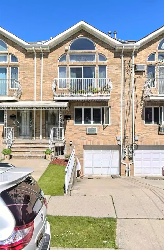 exterior space featuring a balcony, a garage, brick siding, and driveway