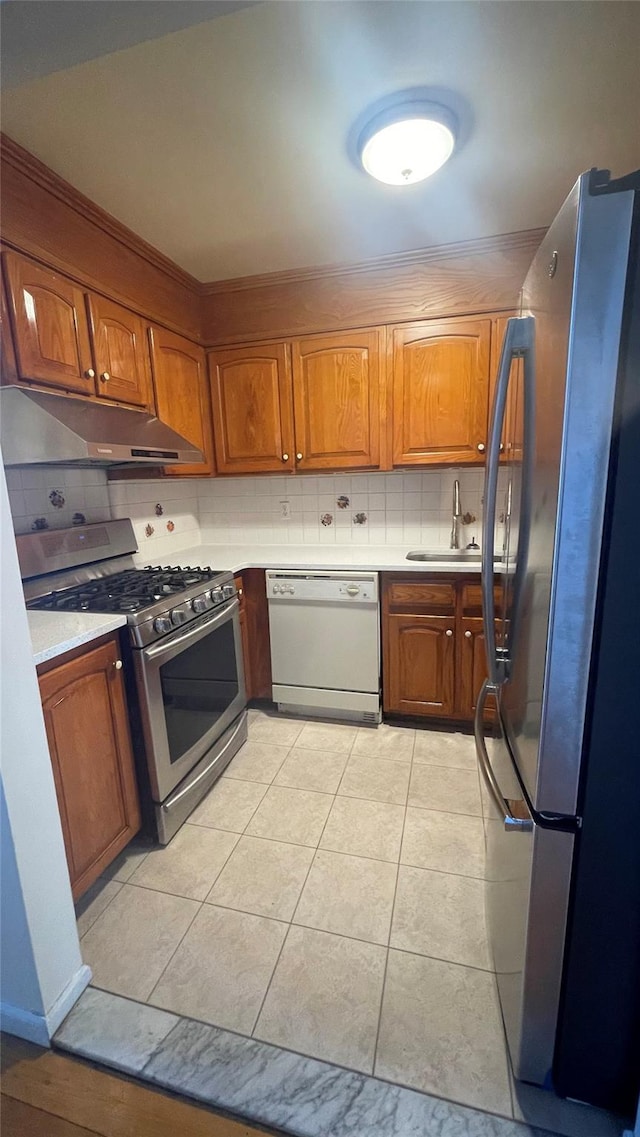 kitchen featuring brown cabinets, under cabinet range hood, a sink, appliances with stainless steel finishes, and light countertops