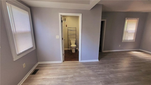 unfurnished bedroom featuring visible vents, baseboards, wood finished floors, and ensuite bathroom