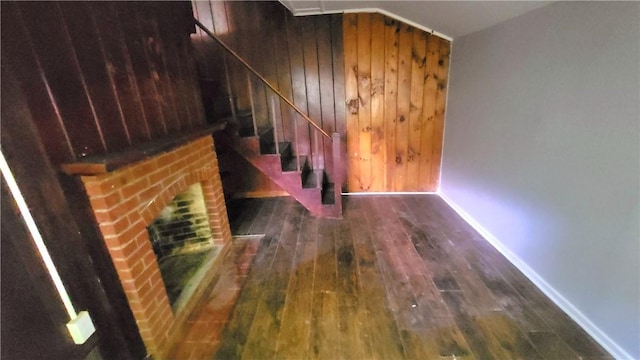 stairs with hardwood / wood-style flooring, wooden walls, a fireplace, and baseboards