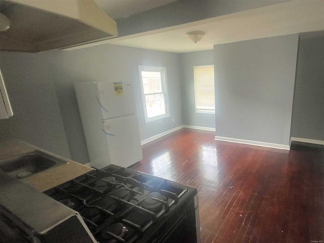 interior space featuring baseboards, black gas range, freestanding refrigerator, wood finished floors, and a sink