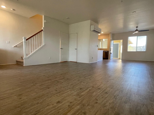 unfurnished living room with an AC wall unit, stairs, ceiling fan, and wood finished floors