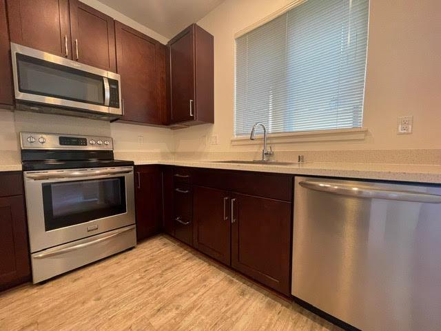 kitchen with a sink, light wood-style floors, appliances with stainless steel finishes, dark brown cabinetry, and light countertops