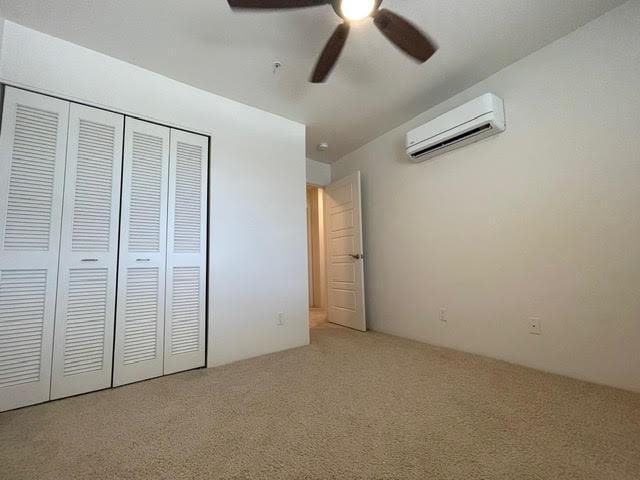 unfurnished bedroom featuring a closet, carpet, ceiling fan, and a wall unit AC