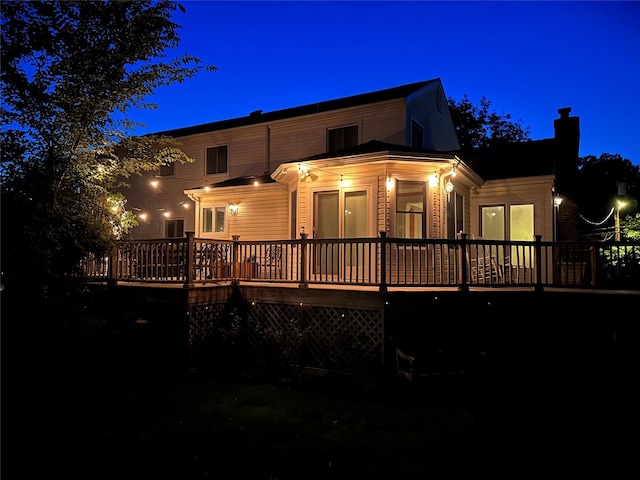 back of house at twilight featuring a deck and a chimney