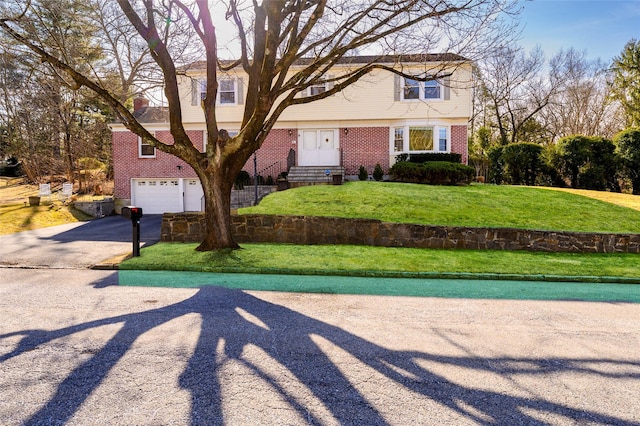 colonial inspired home featuring a front lawn, an attached garage, brick siding, and driveway