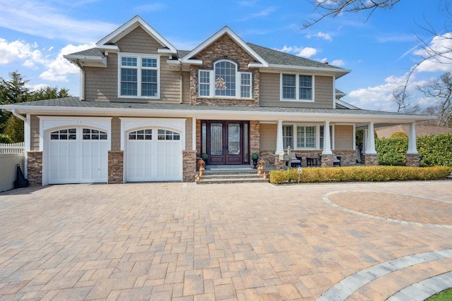 view of front of house featuring decorative driveway, stone siding, fence, french doors, and an attached garage