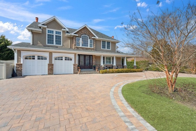 view of front of house with fence, a chimney, a garage, stone siding, and decorative driveway