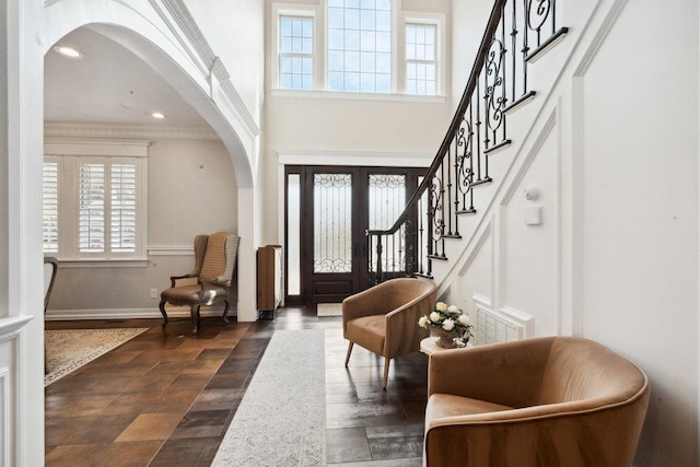 entrance foyer with arched walkways, a high ceiling, stairs, and baseboards